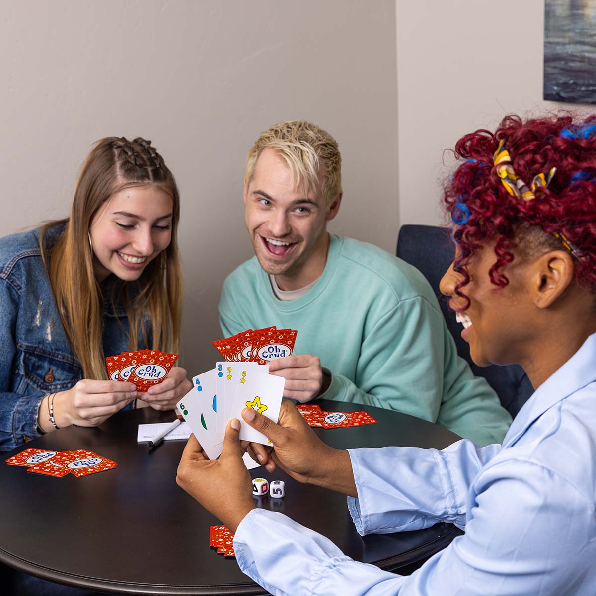 Three friends laughing and having fun as they play Oh Crud, the card and dice game.